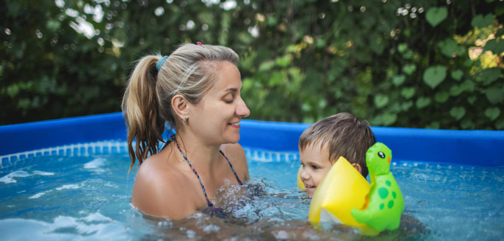 Mum supporting a young boy in a paddling pool. The boy is swimming with arm bands and smiling