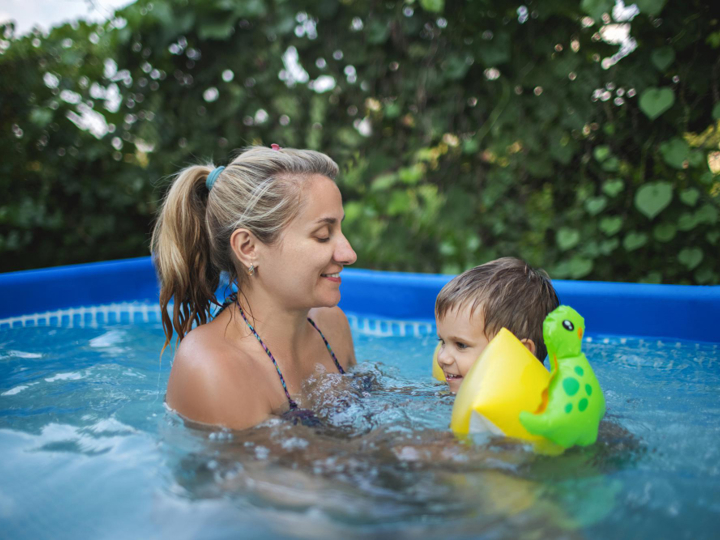 Mum supporting a young boy in a paddling pool. The boy is swimming with arm bands and smiling