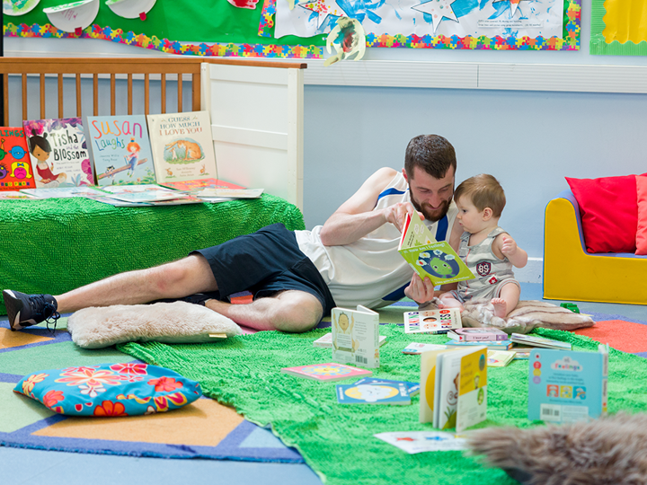 dad and toddler reading a book on the floor in a library