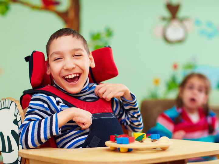 Young boy with cerebral palsy laughing whilst sitting in a chair with a toy in front of him