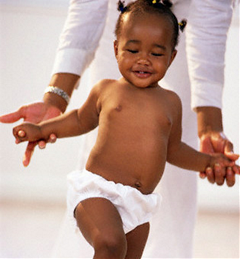 Baby in nappy stepping forward with support from adult holding hands