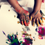 Young child's hands covered in different colour paints and pressing their hands against some pieces of paper. 