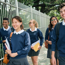 Five teenagers in school uniform smiling and laughing whilst walking down the road.