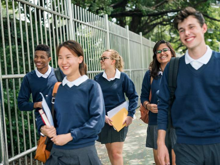 Five teenagers in school uniform smiling and laughing whilst walking down the road.