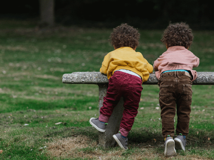 Two black toddlers playing on a bench in a park.
