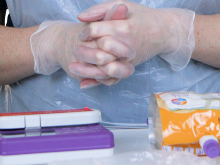 Adult clasping their hands with surgical gloves on behind a table with feeding equipment