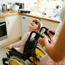 Young girl in a wheelchair smiling up at an adult standing behind her and pushing her wheelchair. Situated in a kitchen