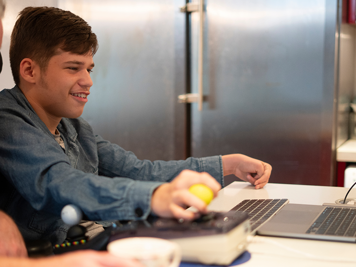 A teenage boy with a disability, sitting in a wheelchair using a laptop