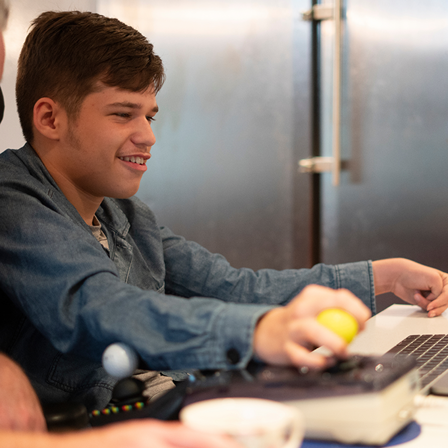 A teenage boy with a disability, sitting in a wheelchair using a laptop