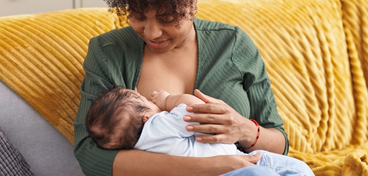 Mum sitting on sofa holding her baby whilst breastfeeding