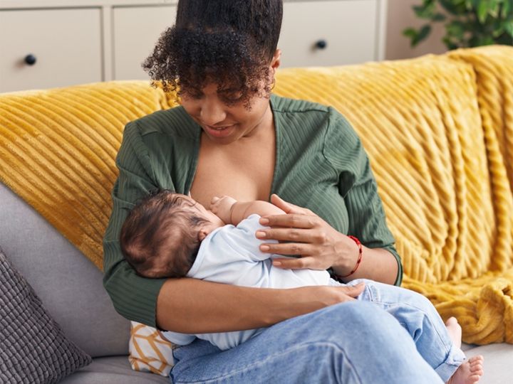 Mum sitting on sofa holding her baby whilst breastfeeding