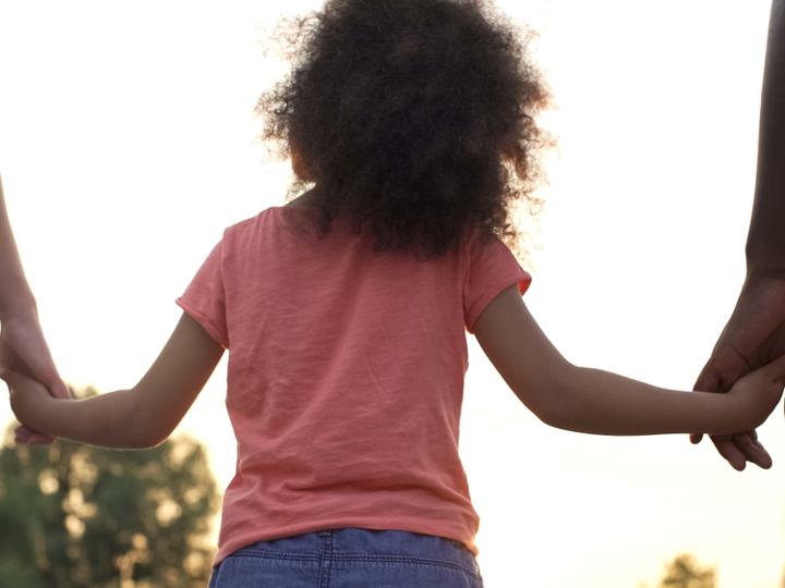 Young girl walking holding hands with two adults either side