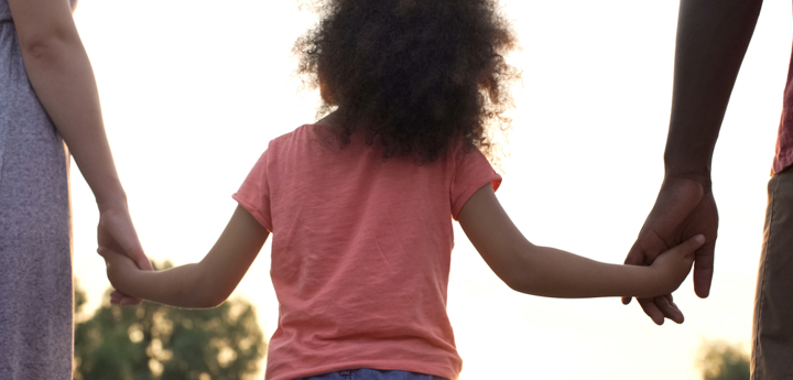 Young girl walking holding hands with two adults either side