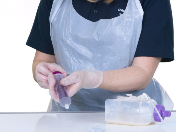 Woman wearing scrubs holding a syringe, with feeding equipment lying on the table in front of her