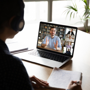 Woman sitting at a table with headphones on a Microsoft Teams call on a laptop.