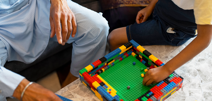 Adult man sitting on sofa and a young boy sitting on the edge of a coffee table, both playing with lego.