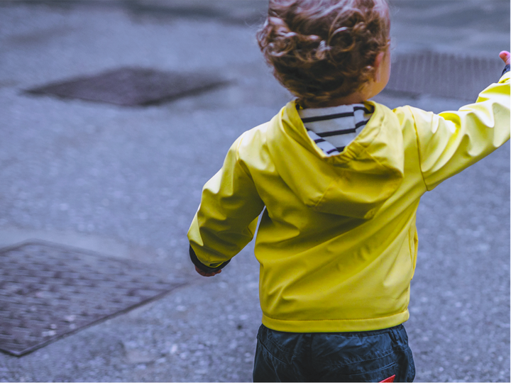 Boy toddler standing near the road in a fluorescent yellow jacket reaching his hand out