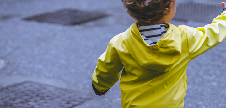 Boy toddler standing near the road in a fluorescent yellow jacket reaching his hand out