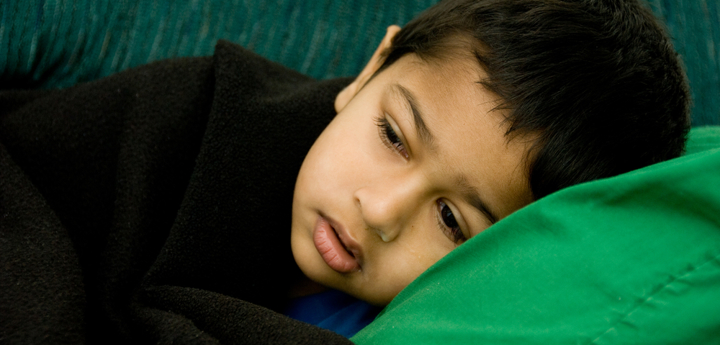 Young boy looking unwell lying on sofa under a blanket