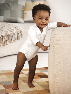 Baby smiling, standing and holding onto arm of sofa
