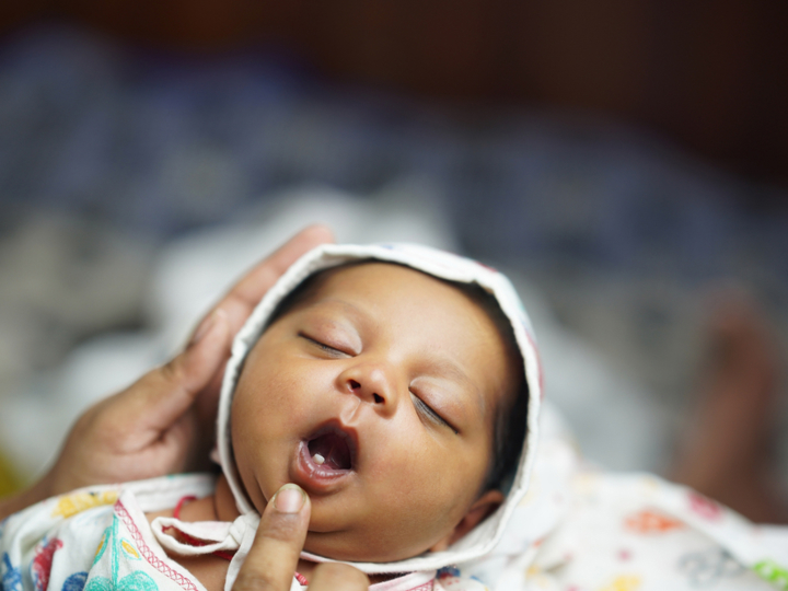 Sleeping newborn baby being held with an adults finger gently pulling down on their lower lip to reveal the baby's first tooth.