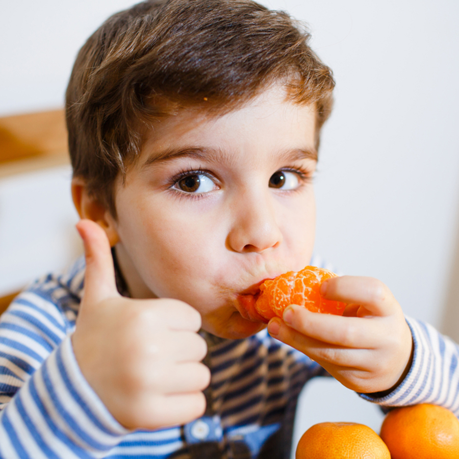 Young boy eating an orange and doing a thumbs up to the camera