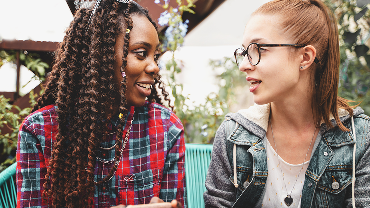 2 teenage girls talking. Girl on left is holding a phone