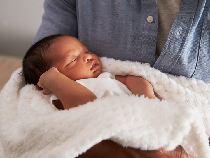 baby asleep in blanket in arms of an adult