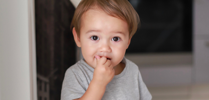 A boy toddler holding his hand up to his mouth