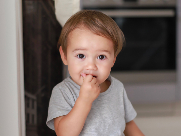 A boy toddler holding his hand up to his mouth