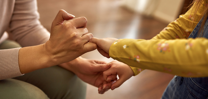 child in yellow long sleeve t-shirt and dungarees holding hands with adult with green trousers and grey jumper