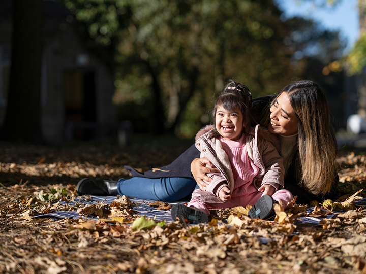Child with down syndrome laughing with a parent in dried leaves