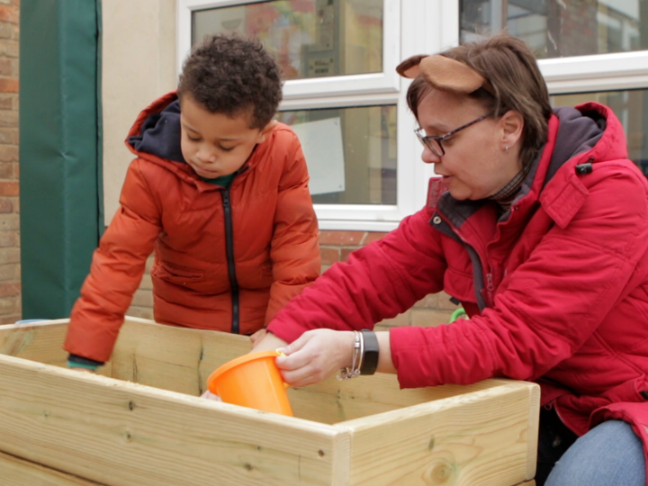 Young boy and teacher playing with a sand pit