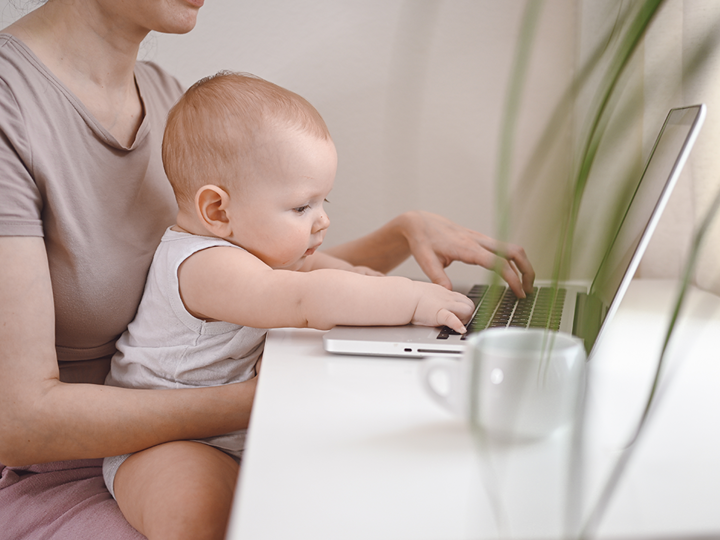 baby typing on laptop whilst sat in adult woman's lap