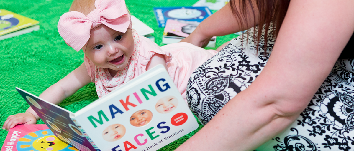 Baby smiling whilst reading a making faces book